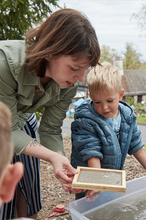 preschool teacher assisting young boy with papermaking activity