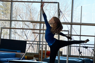 student gymnast in pose with equipment in background