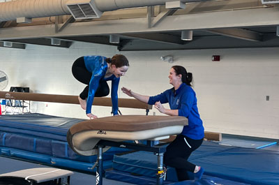 PE teacher spotting student gymnast vaulting