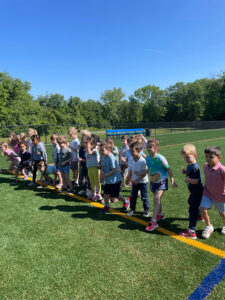 Children lined up on a marking line on the turf field in PE class