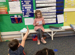 Kindergarten student sounding out letters to friends in phonics 