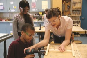 teacher and 2 students in woodshop using hand drill