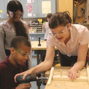 teacher and 2 students in woodshop using hand drill