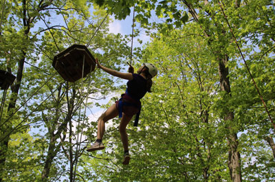 Girl hanging from rope in harness on challenge course