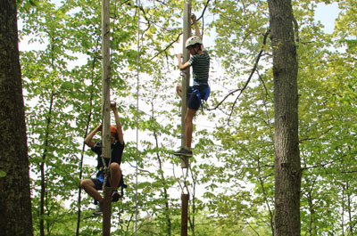 Two boys climbing poles side by side on Renbrook challenge course