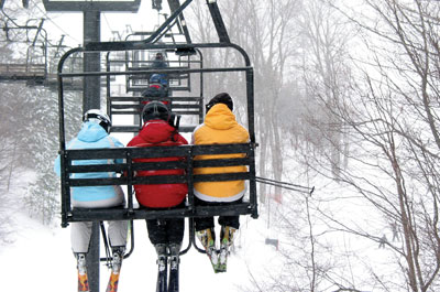 Three skiers on chair lift heading up mountain