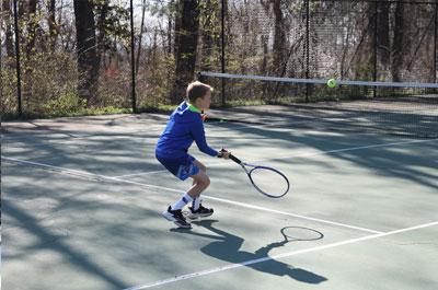 male tennis player hitting ball - photo from behind