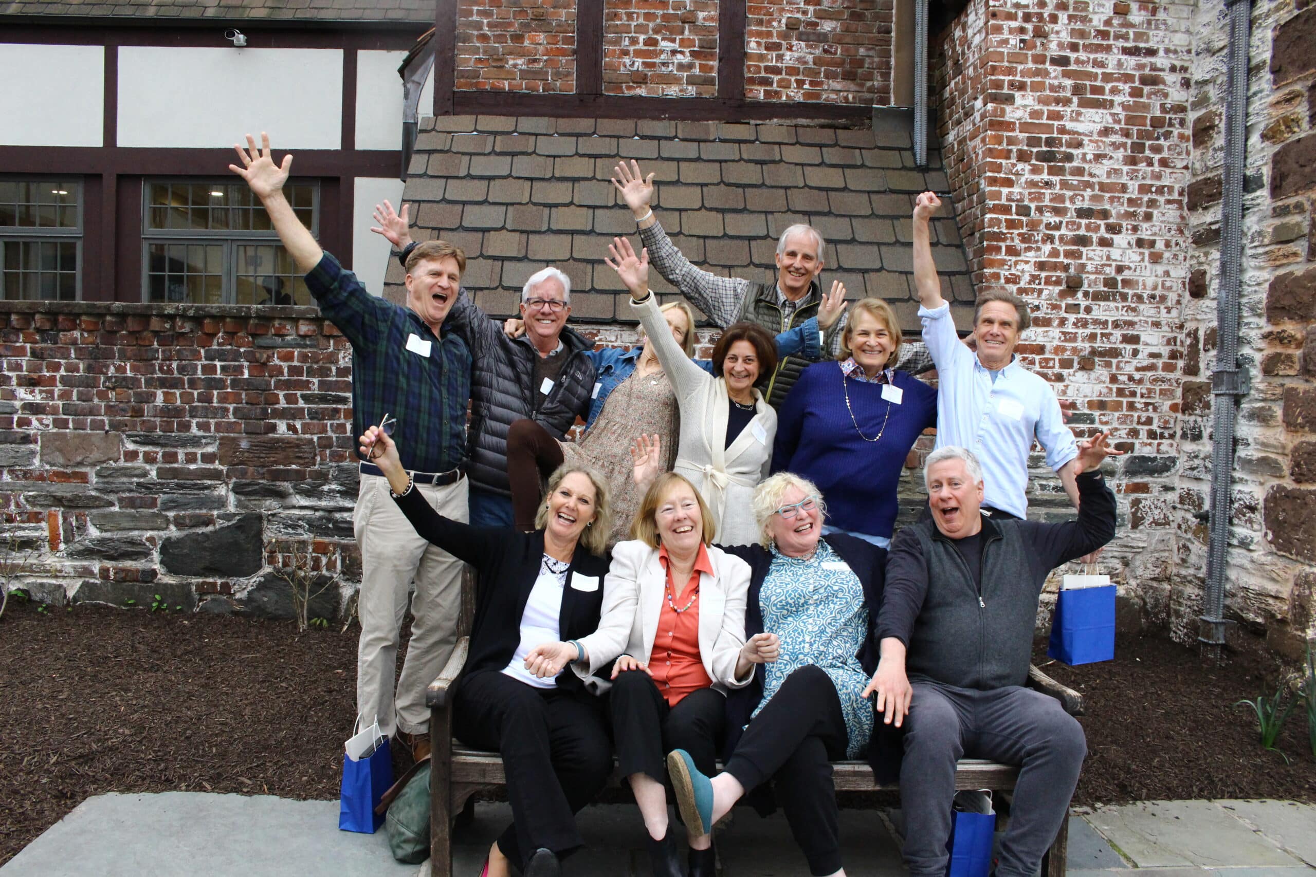 People gathered around a bench for a photo celebrating their 50th middle school class reunion.