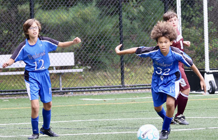 male soccer player dribbling the ball with 2 other boys present