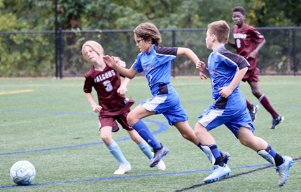 2 male Renbrook middle school soccer players charging forward with ball with 2 opponents
