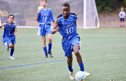3 male soccer players, one in front dribbling the ball