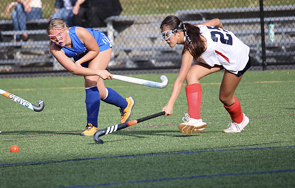 two opposing field hockey girls running after ball
