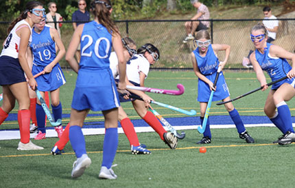 group of 7 middle school girls playing field hockey game