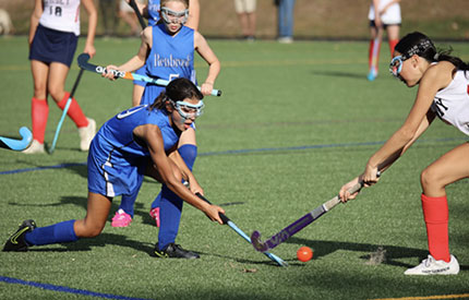 3 girls in field hockey game, 2 battling for control of the ball