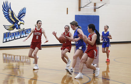 group of middle school female basketball players engaged in a game in Barnes Gym at Renbrook School with Hawks logo on wall