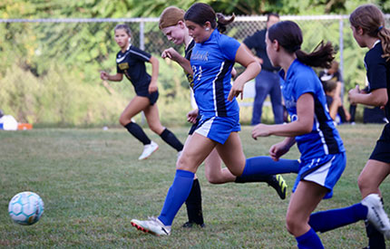 group of female middle school soccer players chasing ball
