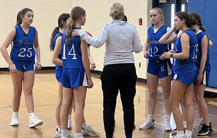 7 female basketball players gathered around Coach Kath Sigrist