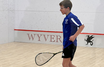 teenage boy on a squash court with a racket