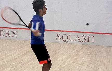 middle school boy hitting a squash ball on a squash court