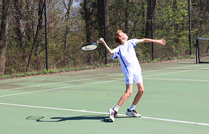 middle school boy on tennis court serving the ball