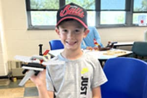 young boy showing a Lego jet he built at camp