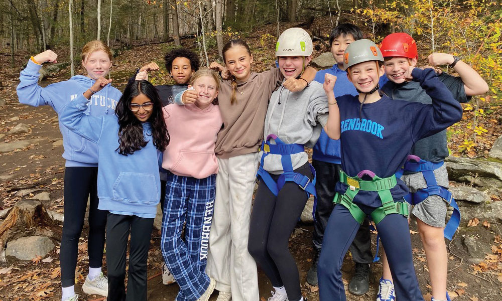 Group of young teen Renbrook middle school students with helmets and harnesses on ready to climb a high ropes element