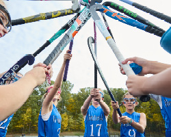 middle school girls field hockey players raising their sticks in a cheer
