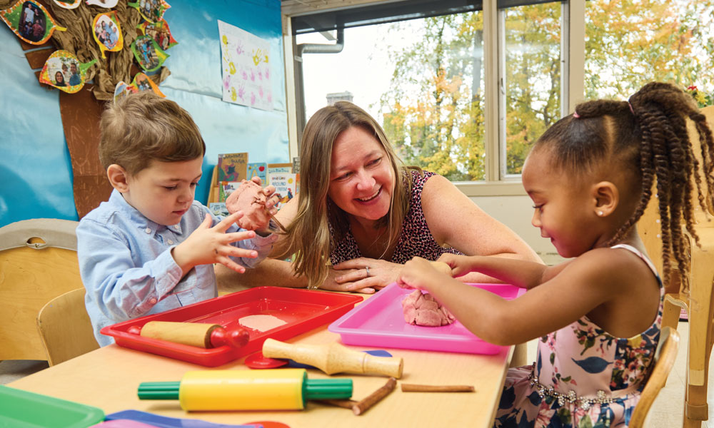 Preschool boy and girl working with clay at Renbrook School while teacher looks on