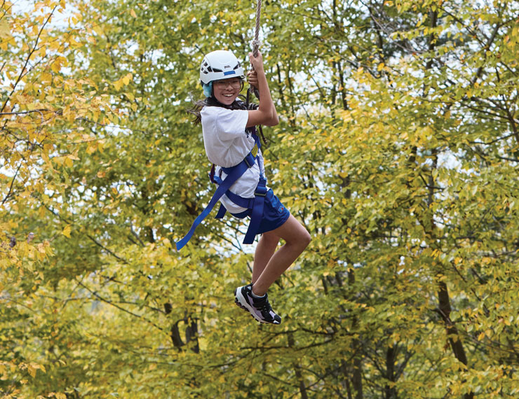 middle school girl bravely swinging through the trees on a challenge course