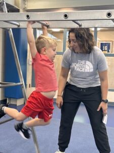 Preschool boy on climbing apparatus in physical education with PE teacher
