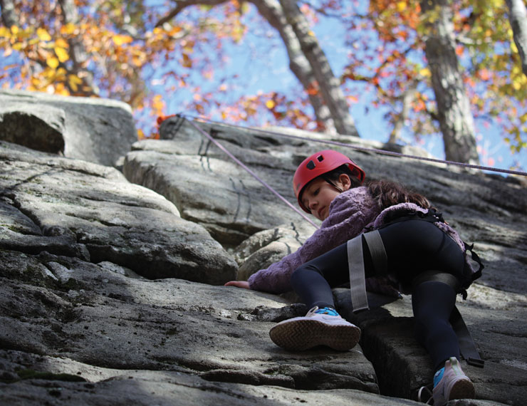 Young girl climbing high rock wall