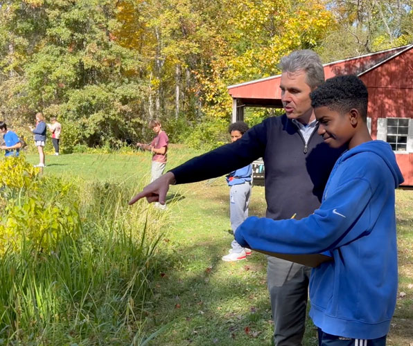 science teacher pointing out vegetation at pond to middle school student