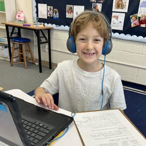 young boy smiling in front of computer with head phones on