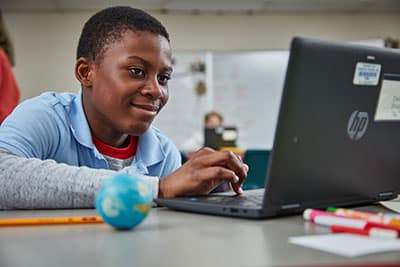black male middle school student smiling at computer with a small globe in the foreground