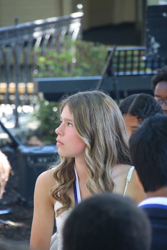 Young woman with long hair listening to graduation speaker