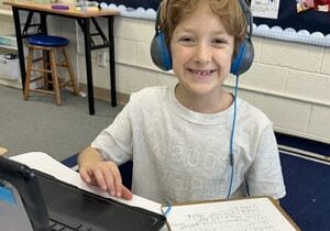 young boy smiling in front of computer with head phones on