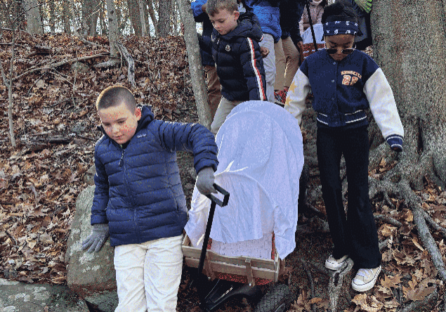 Wagons-in-woods Group of third-grade students pulling covered wagons through the woods