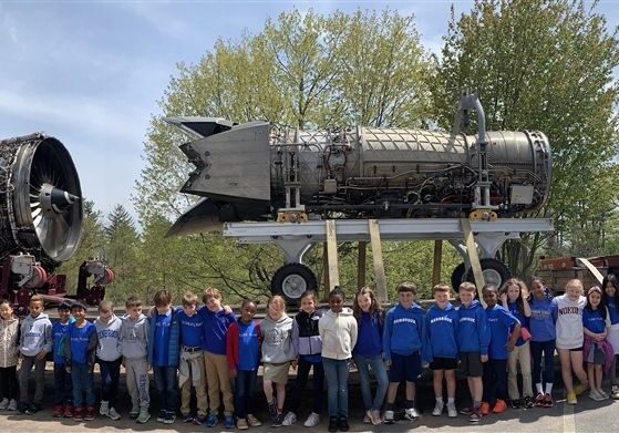 Grade 2 students standing in front of large Pratt & Whitney engine